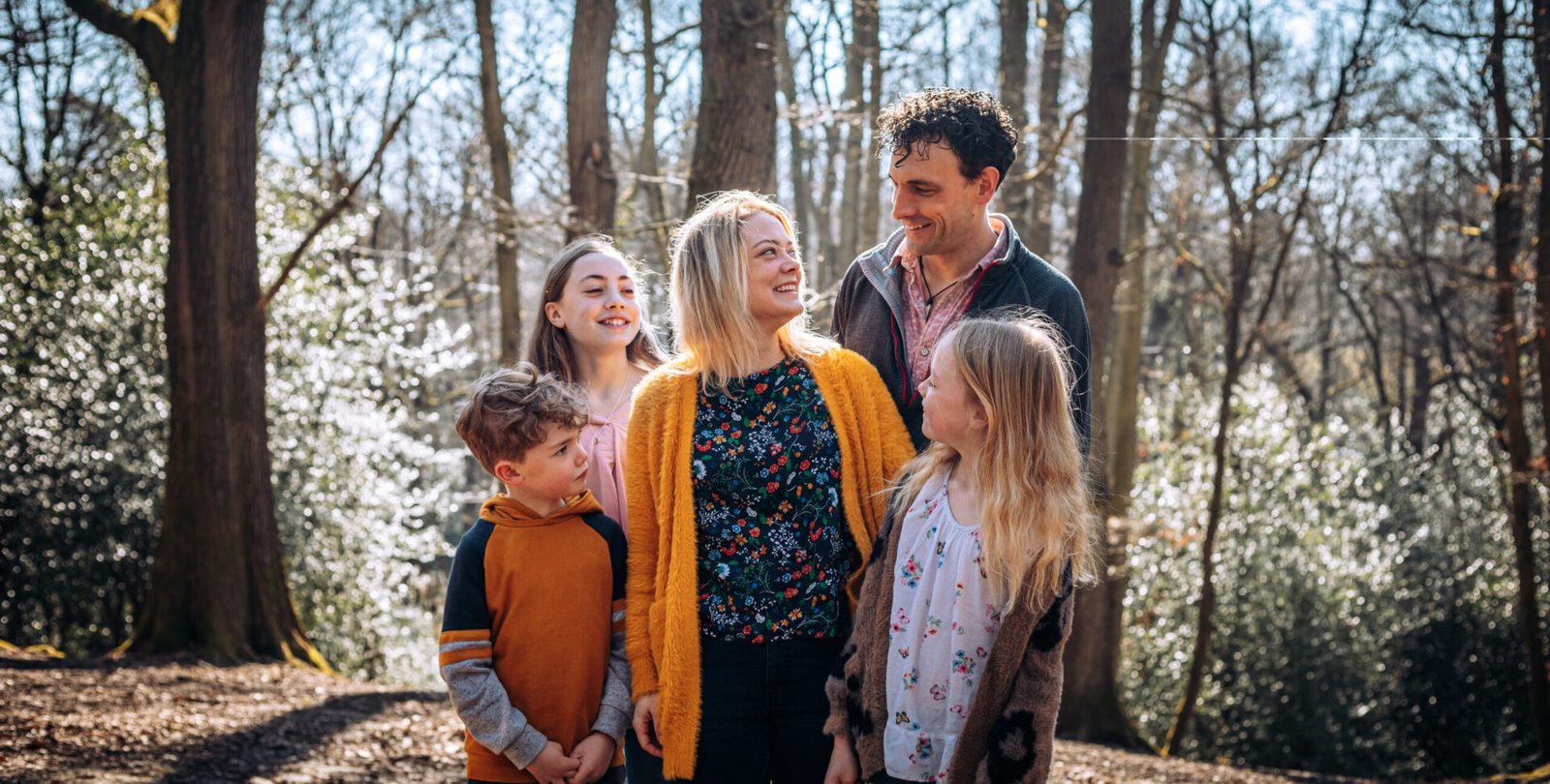 A family of five, surrounding and looking at mum in the woods in Autumn.