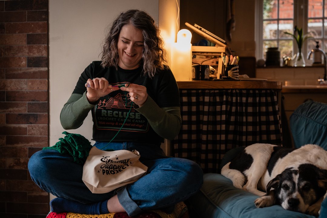 Small business owner, Bex, crocheting in her living room in front of a cosy fire.